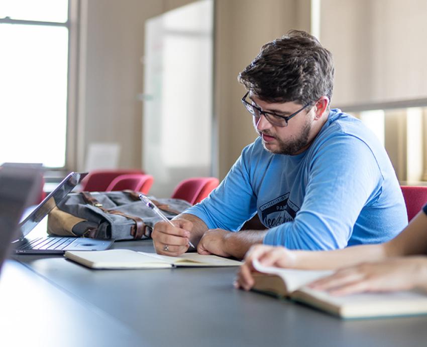 A student in a blue shift writes in a notebook