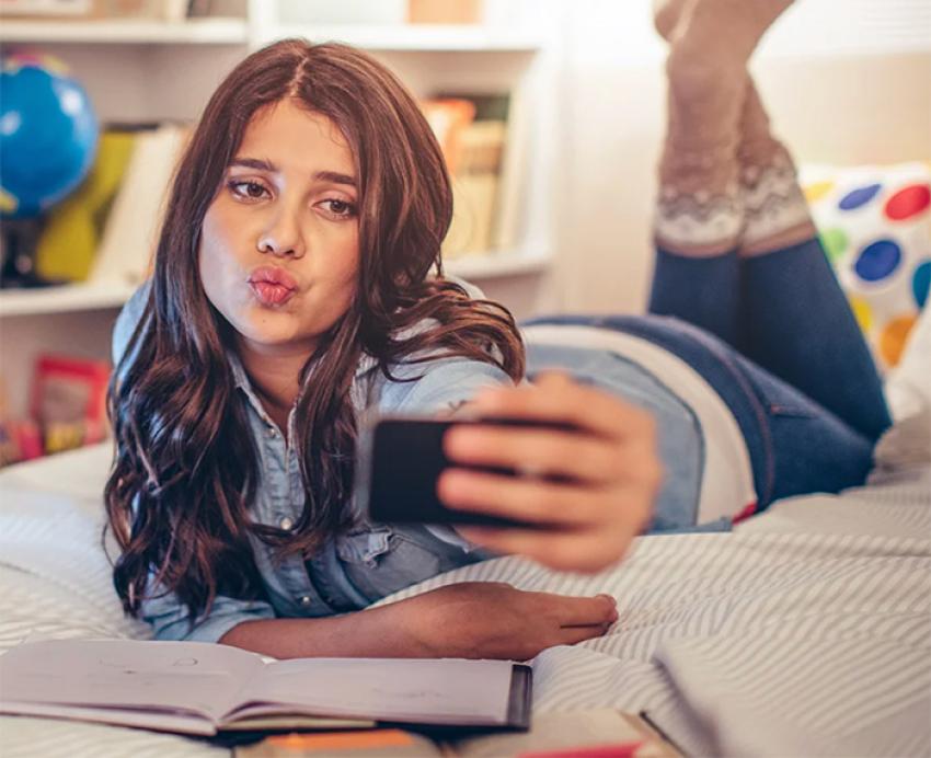 A teenager takes a selfie while lying on a bed