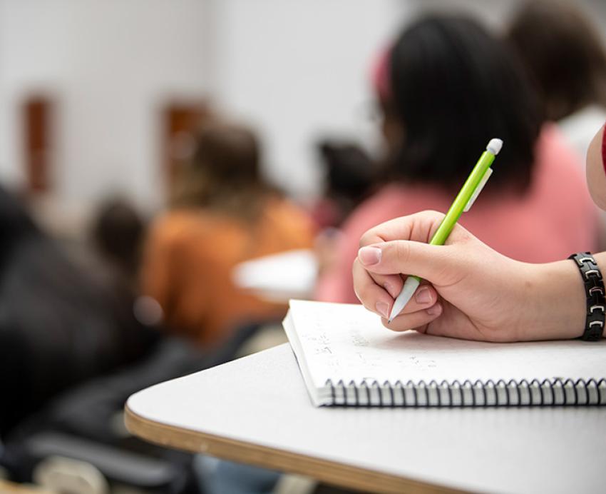 A hand taking notes in a spiral-bound book