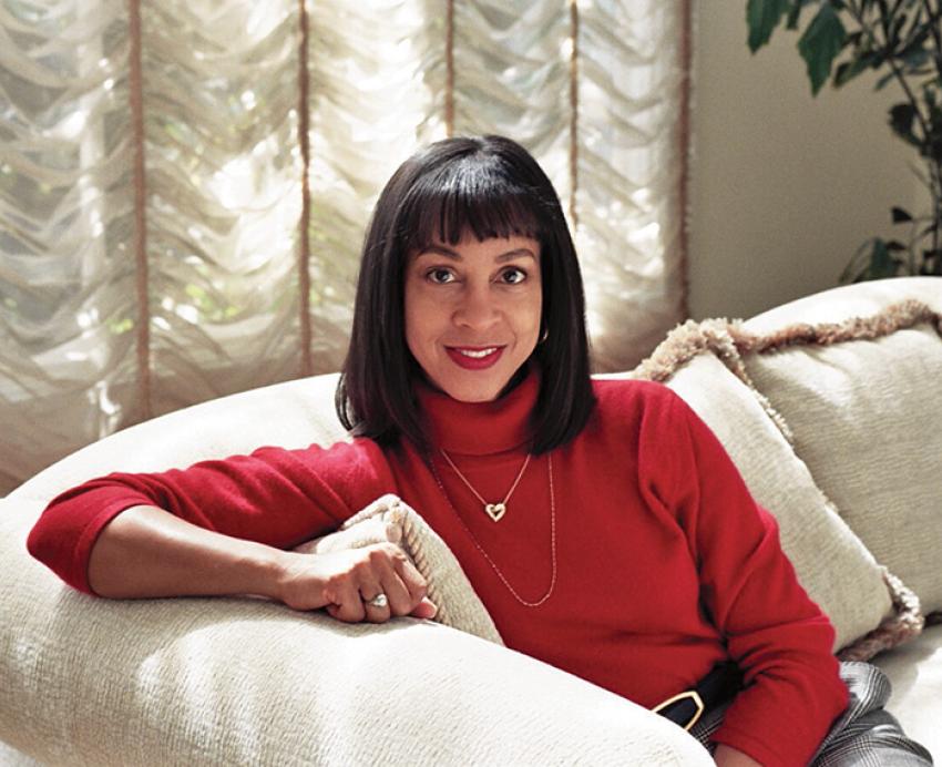 Campbell sits on a couch in a red turtleneck