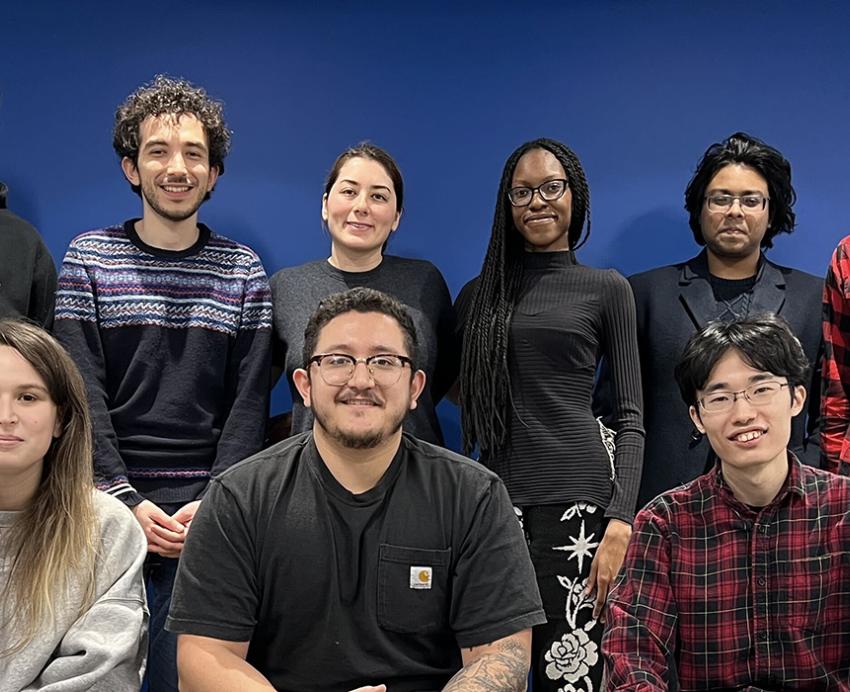 9 people pose against a blue wall