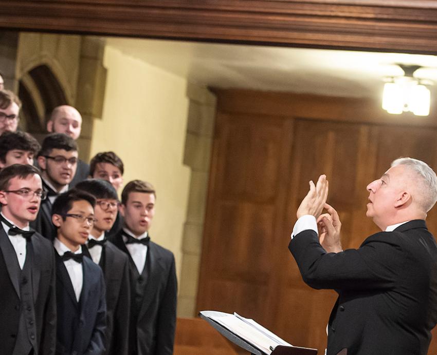 A choir of men in tuxedos are conducted