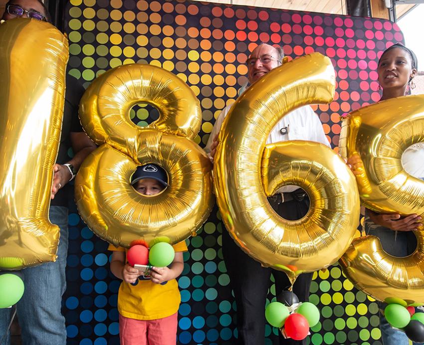 People hold up gold number balloons that spell out 1865