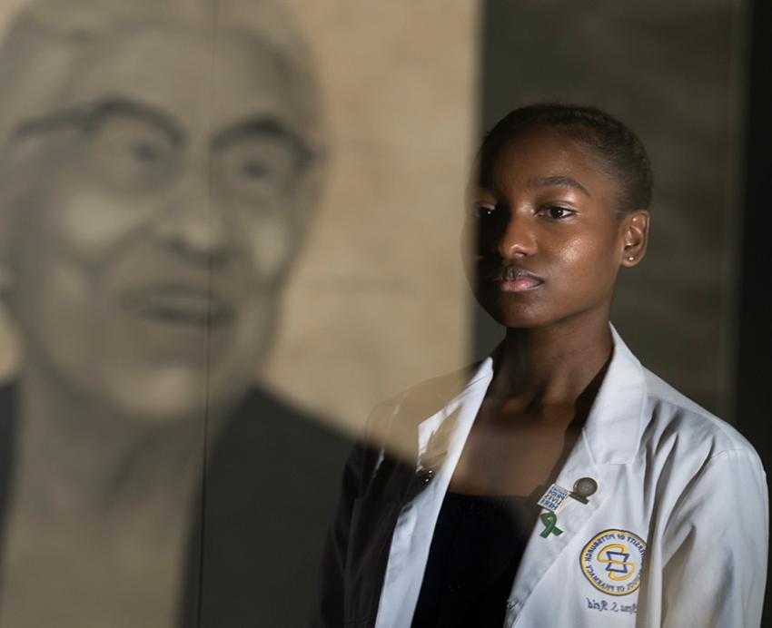 Two people in white coats stand in front of a portrait of Ella P Stewart