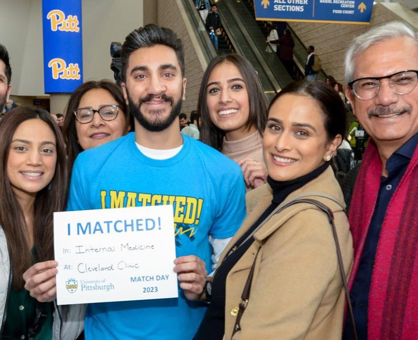 A person in a blue shirt surrounded by family members holds up a sheet of paper that reads I matched