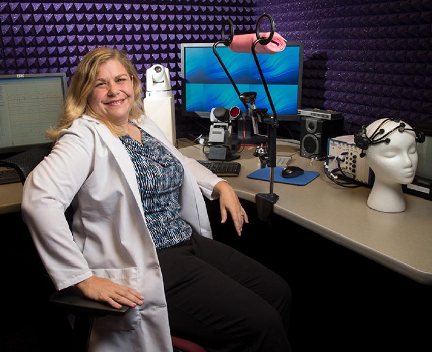 Kymberly Young sits at a desk surrounded by equipment