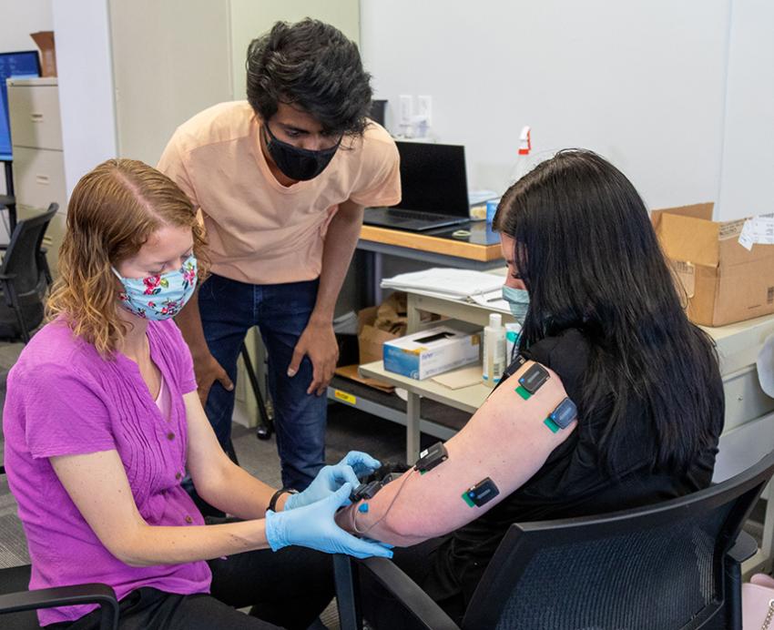 Two people attach electrodes to the arm of a person in a black shirt