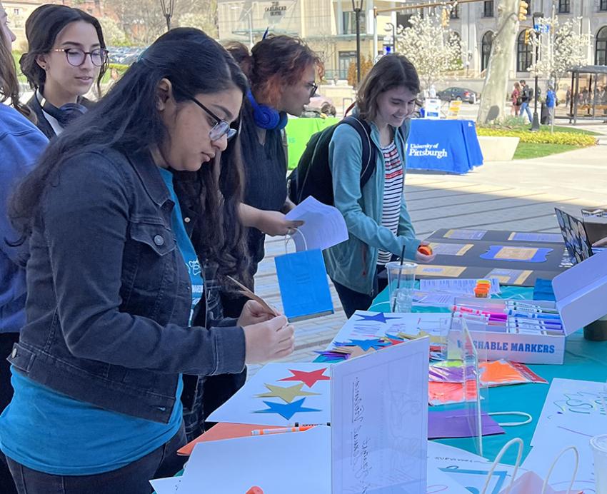 People sitting at a table show art supplies to a group standing across from them