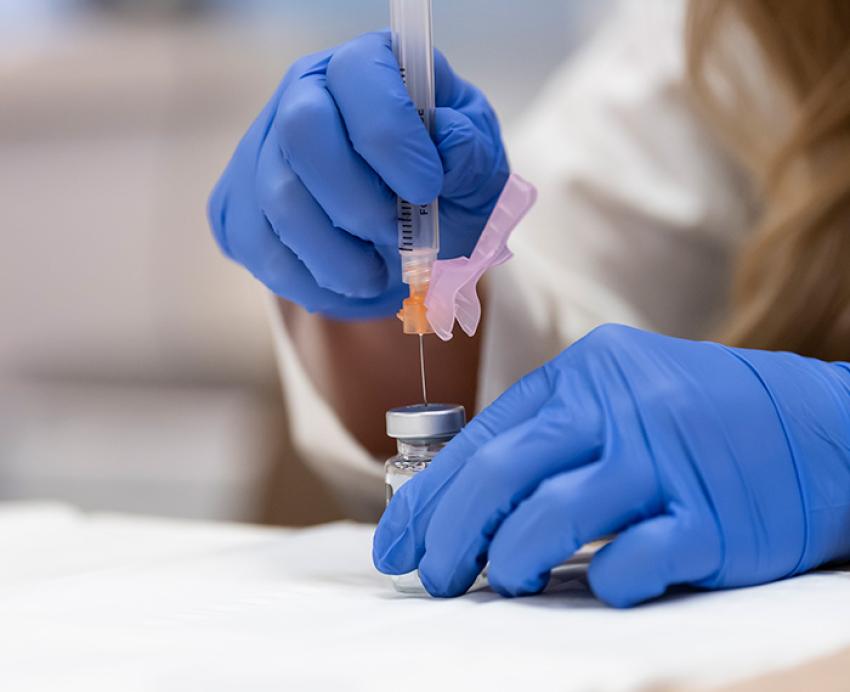 Gloved hands pull a vaccine into a syringe