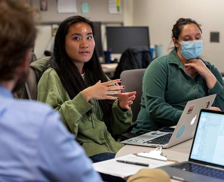 A person in a green shirt talks to others at a conference table
