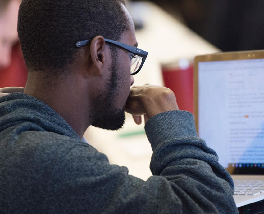 A person in a black hoodie looks at a laptop screen
