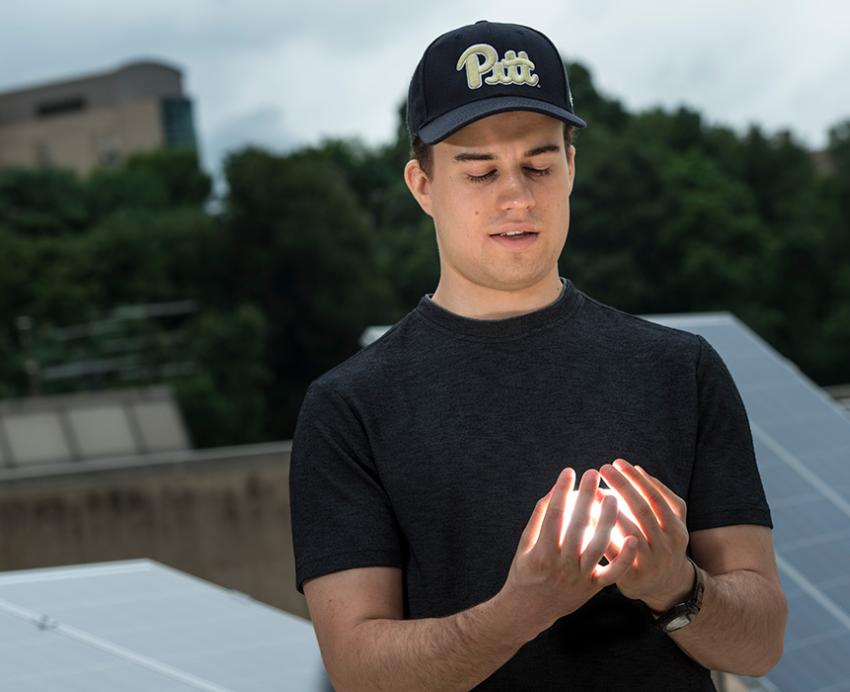 Senior Sam Ressin standing in front of an array of solar panels, with a glowing object in his hands