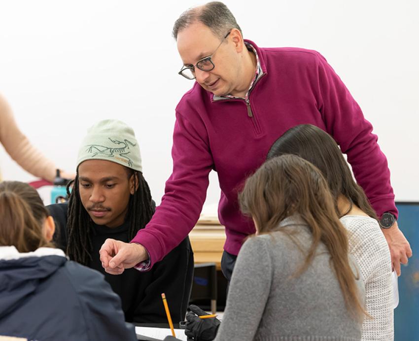 A professor assists a group of students sitting at a table