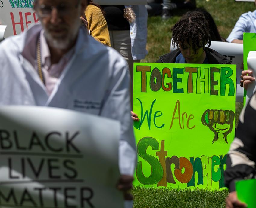 A person holds a green sign that says together we are stronger. Doctors holding signs stand around them.