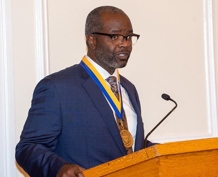 John Wallace speaks at a podium wearing a medal