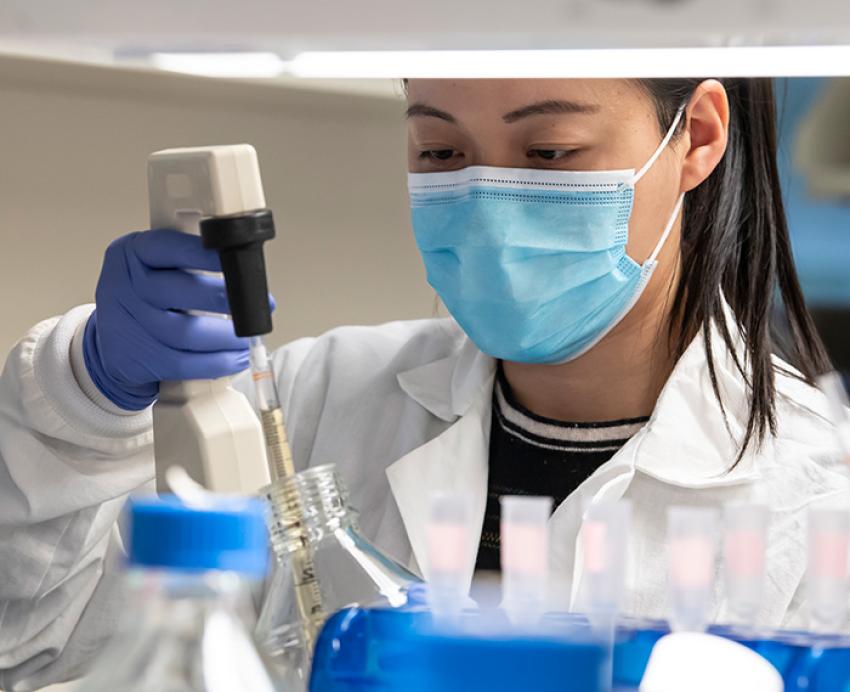 A researcher in a mask uses a pipette in the lab