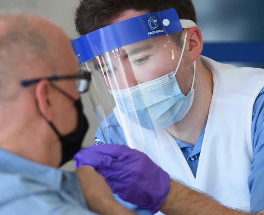 A doctor in a mask and a face shield gives a vaccine to a masked man
