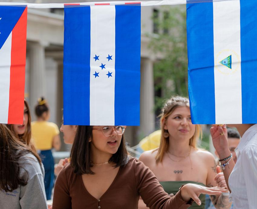 People talk and eat behind flags of Latin American countries hanging in the foreground