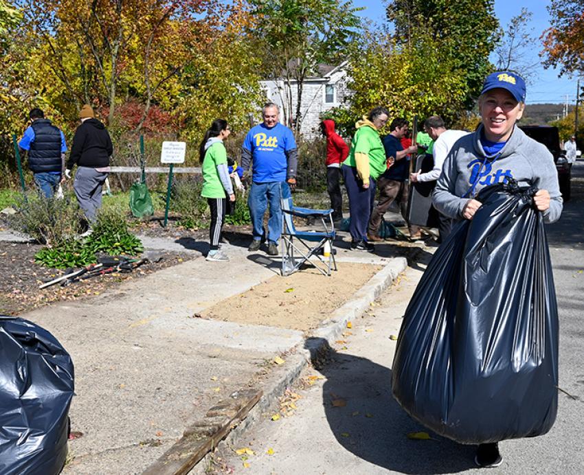 A person in a Pitt hat and shirt holds up a black trashbag