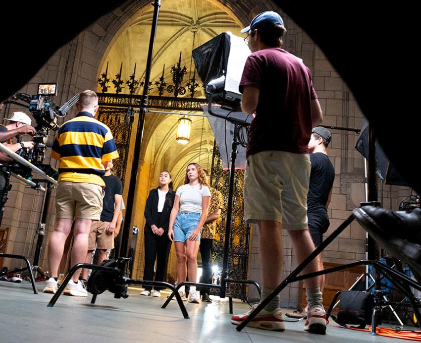A crew with cameras and lighting equipment films actors in the Cathedral of Learning