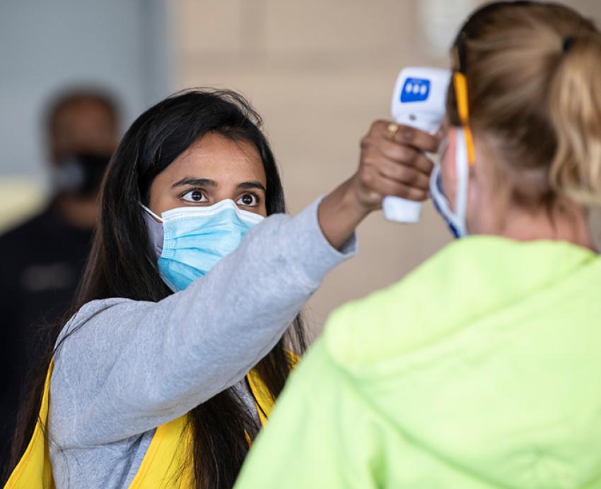 A person in a mask takes another person's temperature with a hand-held thermometer