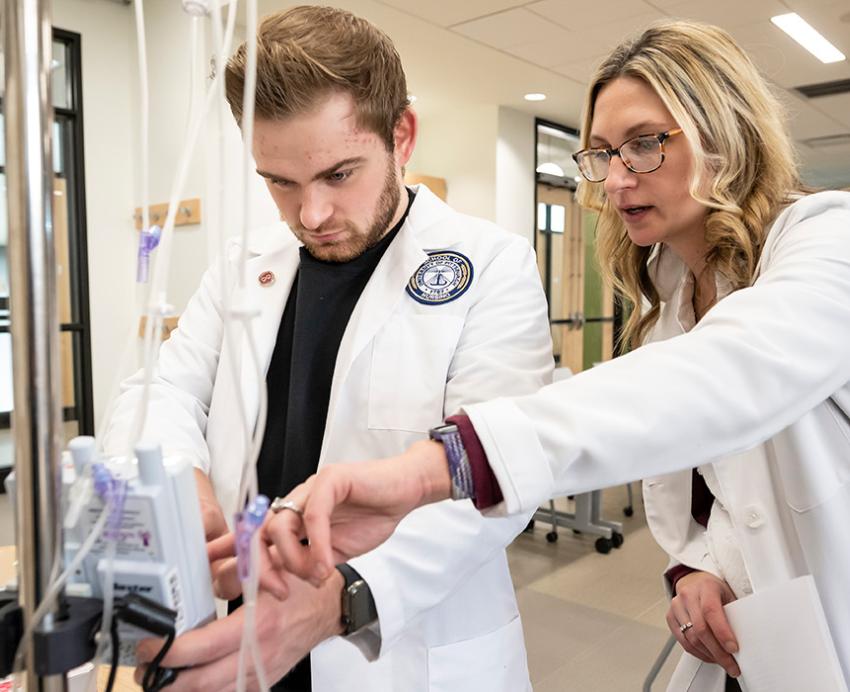 Two nurses in white coats work on an IV stand