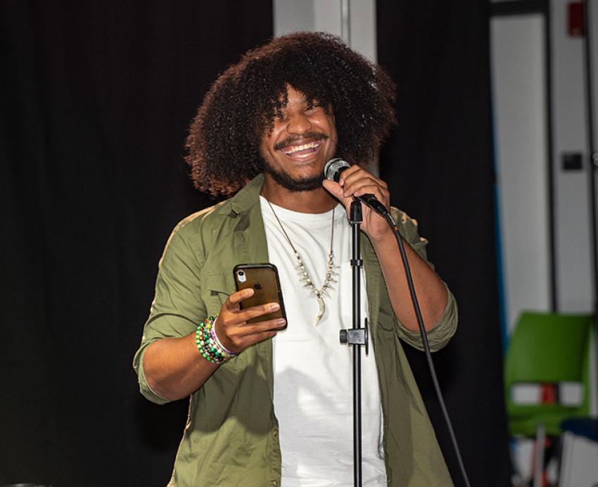 A person holds a phone and laughs at a microphone