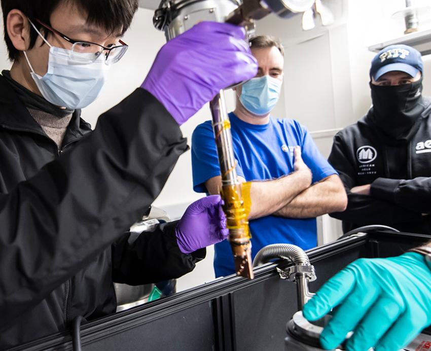 People gather around a machine that makes quantum computing parts
