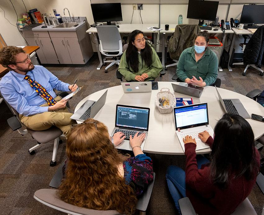 Six people sit around a table with laptops