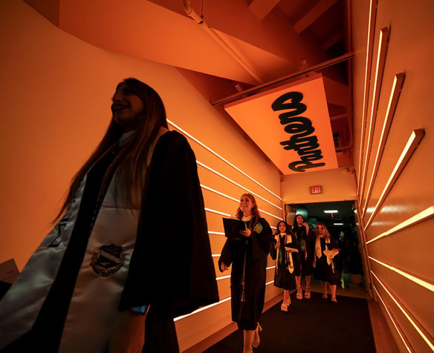 Graduates walk down an orange hallway