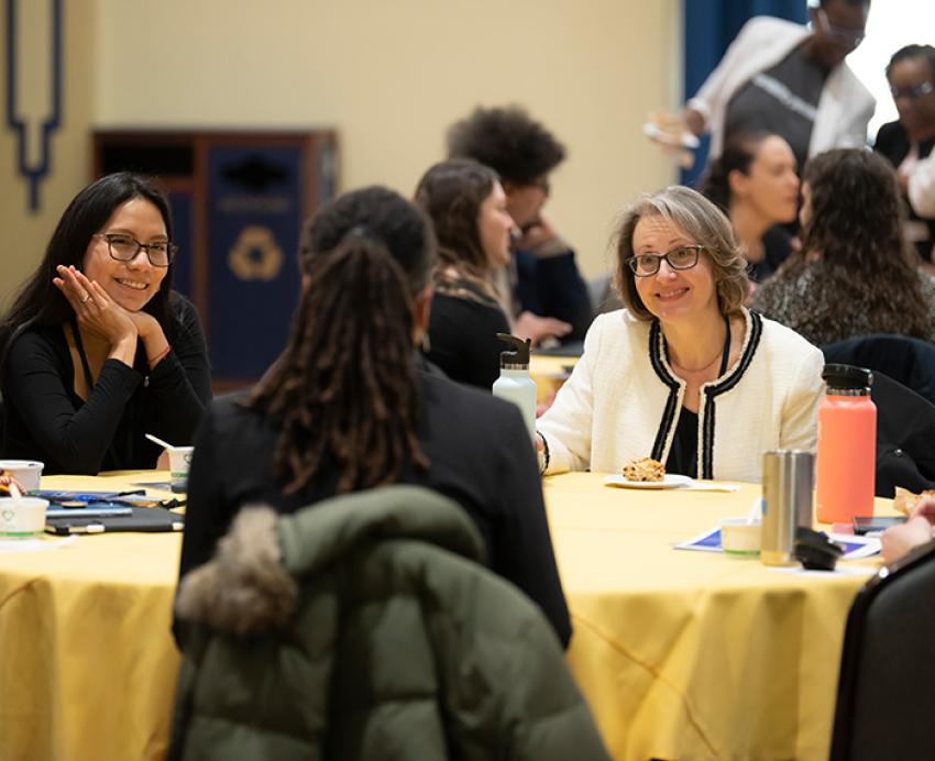 People talk around a table with a yellow tablecloth