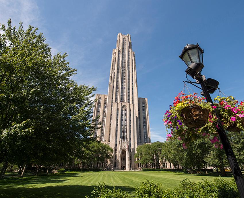 Flowers hang from a lamppost in front of the Cathedral of Learning