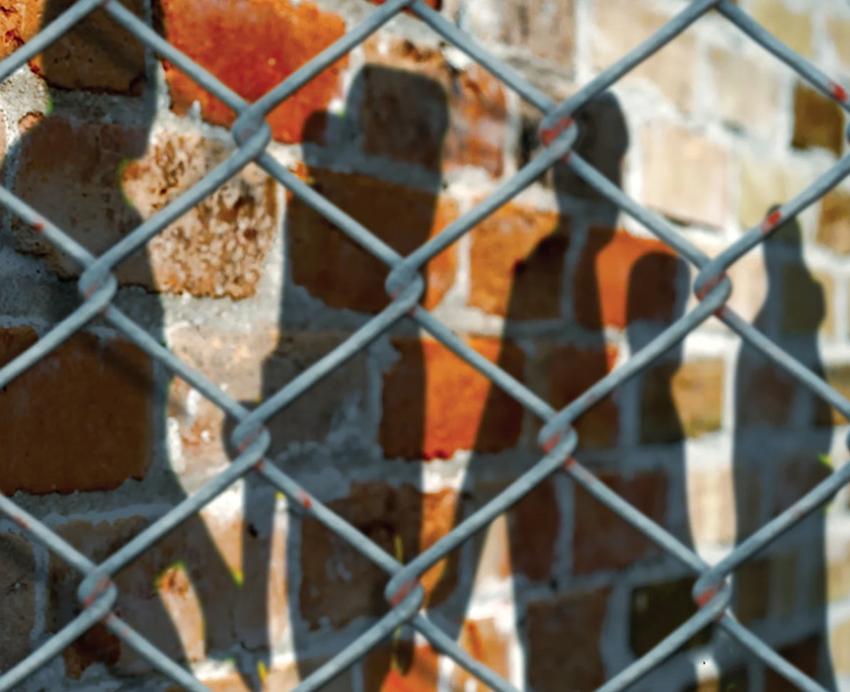 Shadows on a brick wall behind a chain-link fence