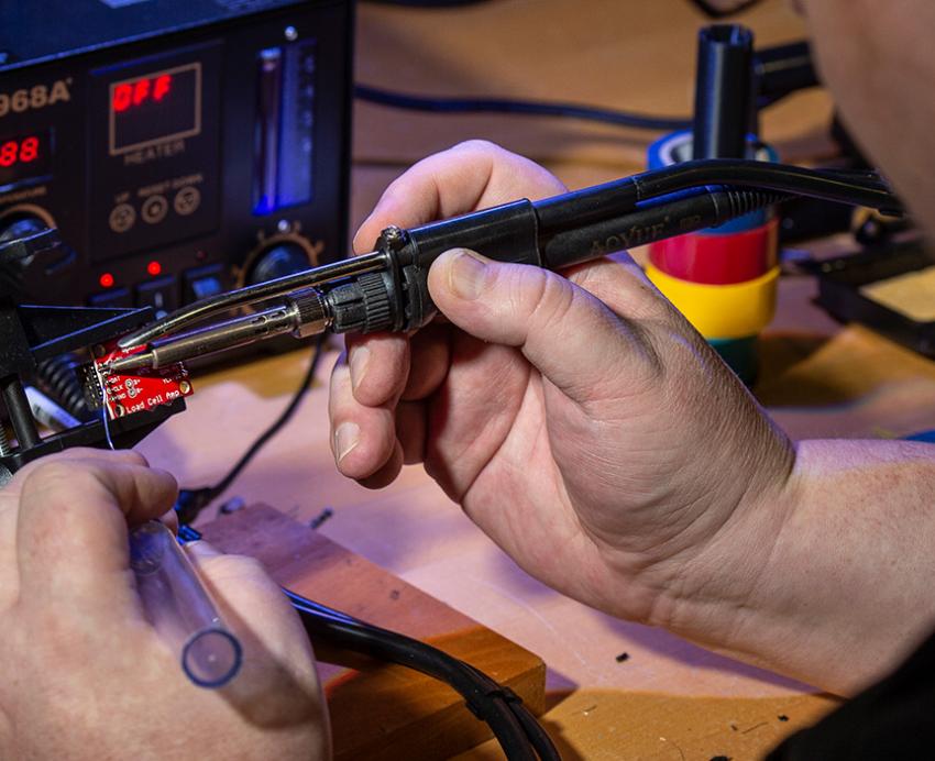 A person uses tools on a small metal chip