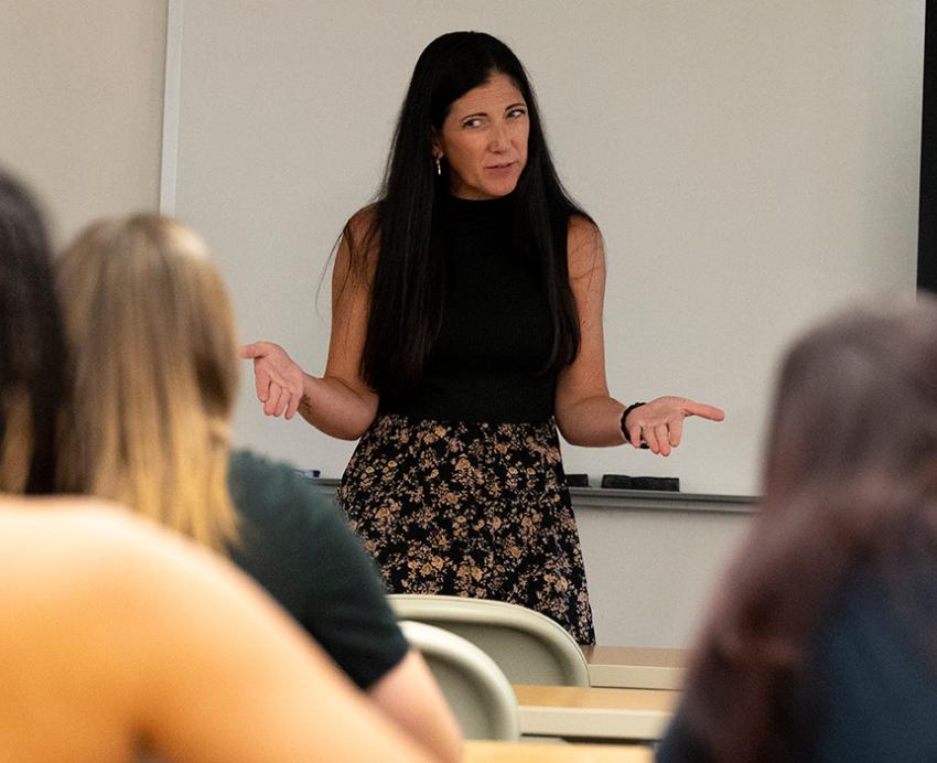 A professor gestures in front of students sitting in rows of desks
