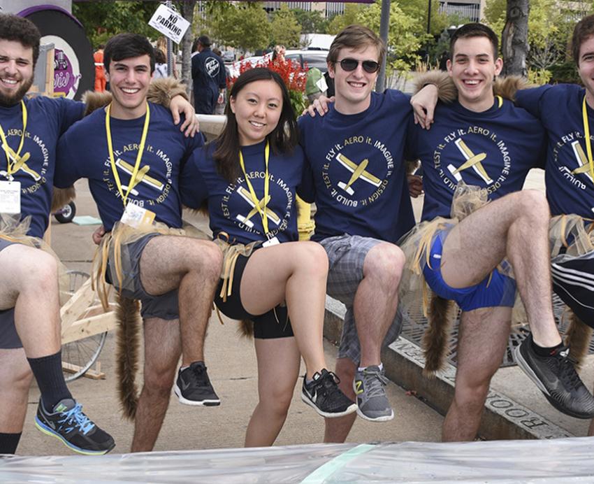 A group of students poses with their legs raised in the air