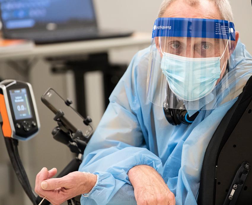 A masked person looks back from a wheelchair with mounted devices