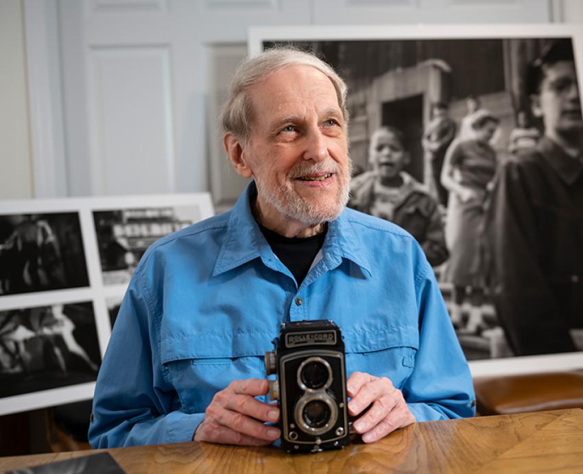 Rosella sits with his camera in front of photographic prints