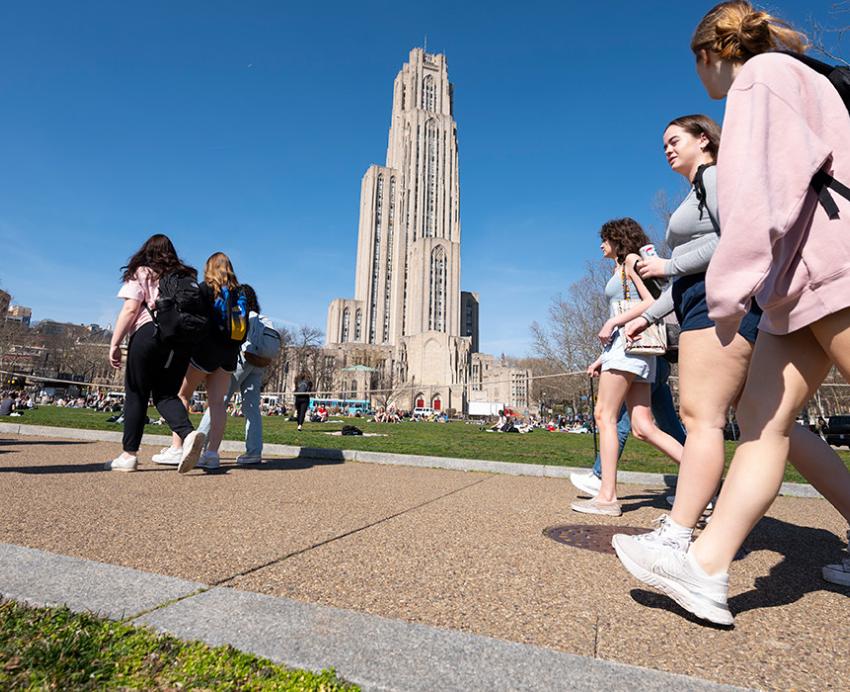 Groups of students walk by Schenley Plaza, with the Cathedral of Learning in the background