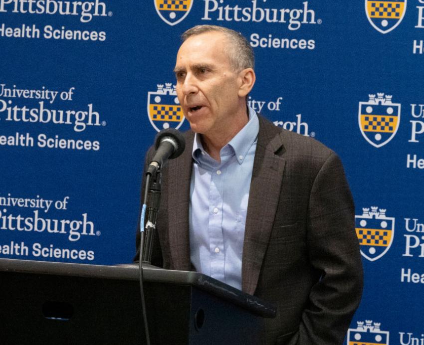 Michel Boninger speaks in front of a Pitt Health Sciences logo 