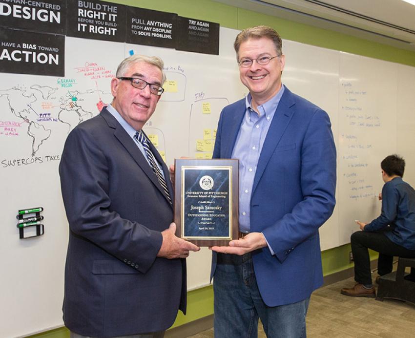 Two men in suits hold a plaque