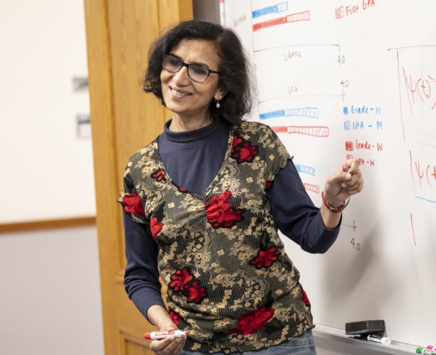 Chandralekha Singh, holding a marker, points at a whiteboard with graphs on it.