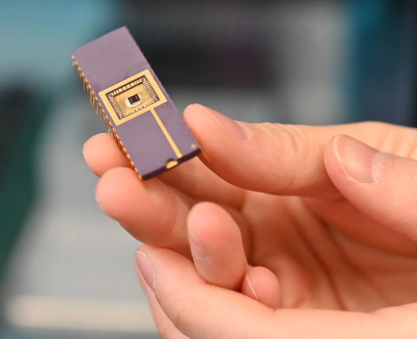 A hand holding a small chip that has gold circuits on the surface