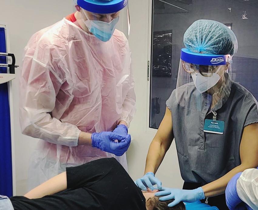 Two people in personal protective gear examine a patient's ear