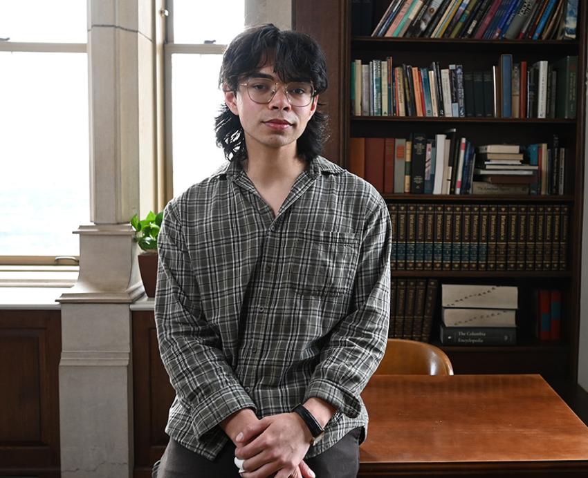 Diaz leans on a table near a bookshelf
