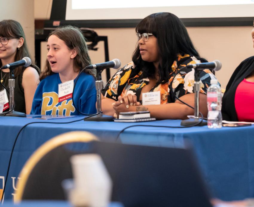 A panel of four people sit at a table with microphones