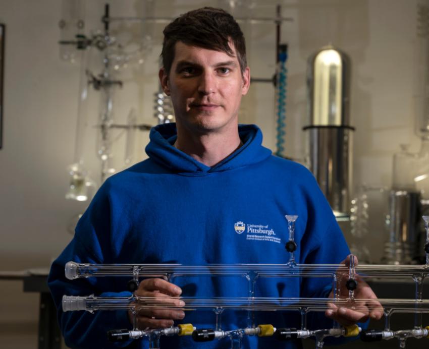 Ryan Tate poses with an apparatus of glass tubing