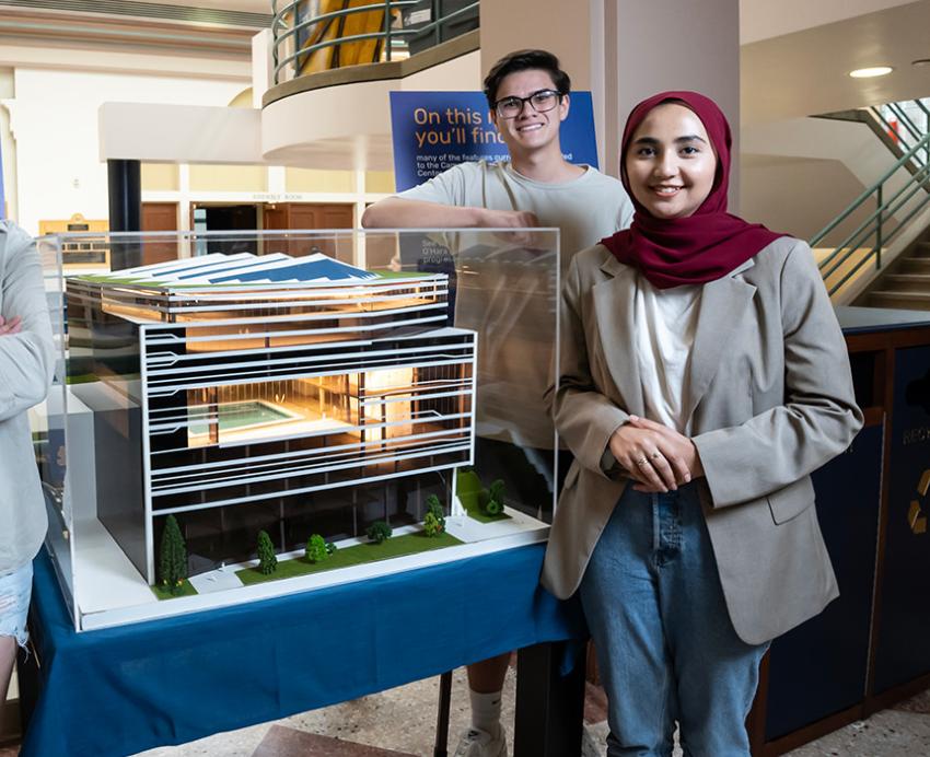 Four students stand around their model behind glass