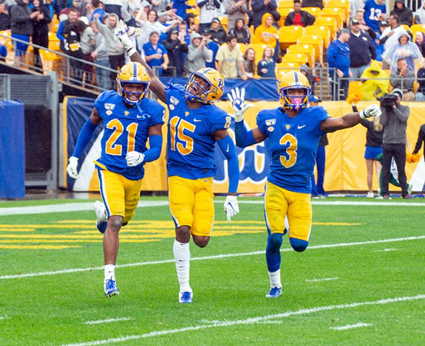 Three Pitt football players wave as they run on the field