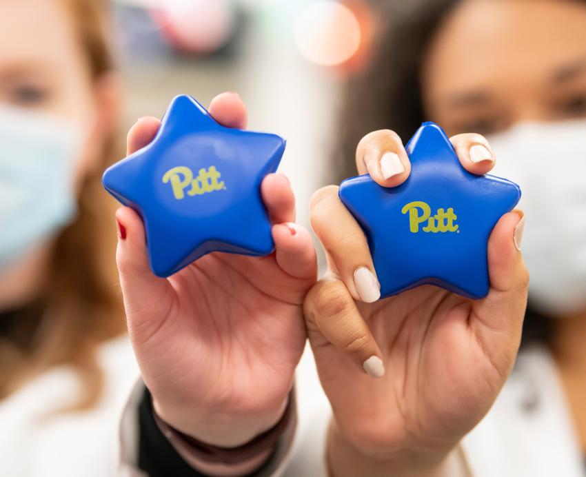 Two people hold up blue photo stars with the text "Pitt."